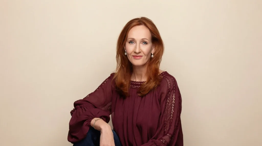 J.K. Rowling at a writing desk, warm library setting, smiling softly.