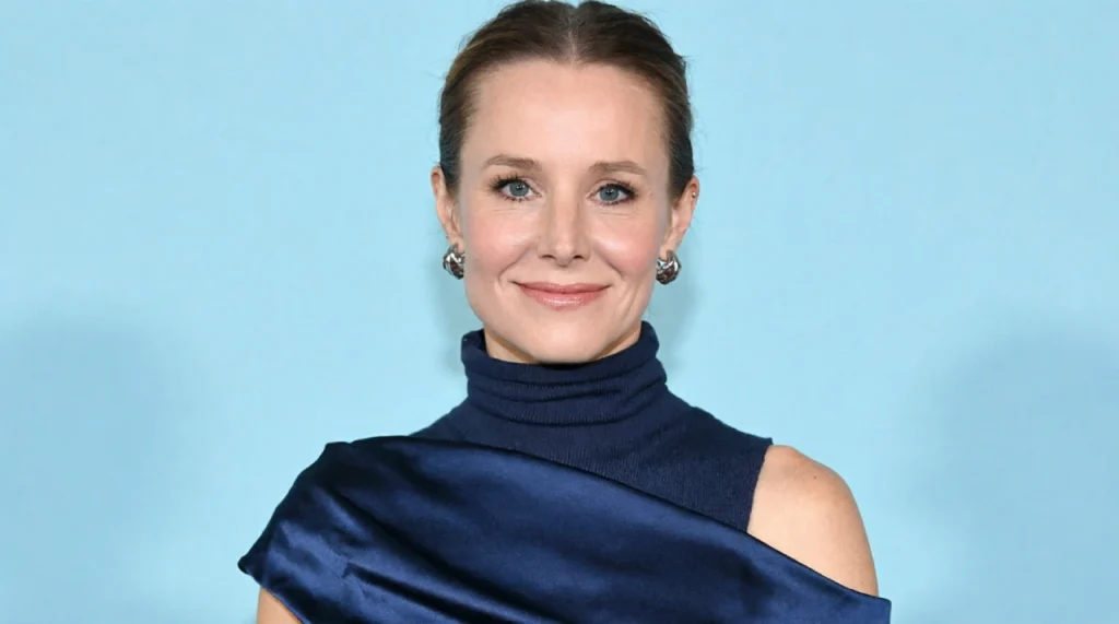 Kristen Bell smiling brightly, floral top, warm lighting.