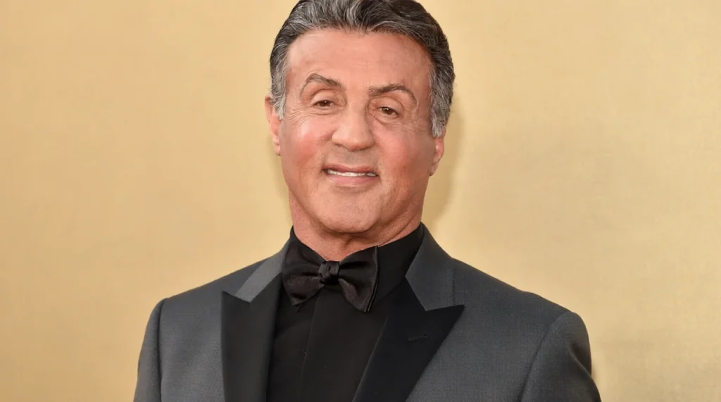Sylvester Stallone looking determined, wearing a black tank top.